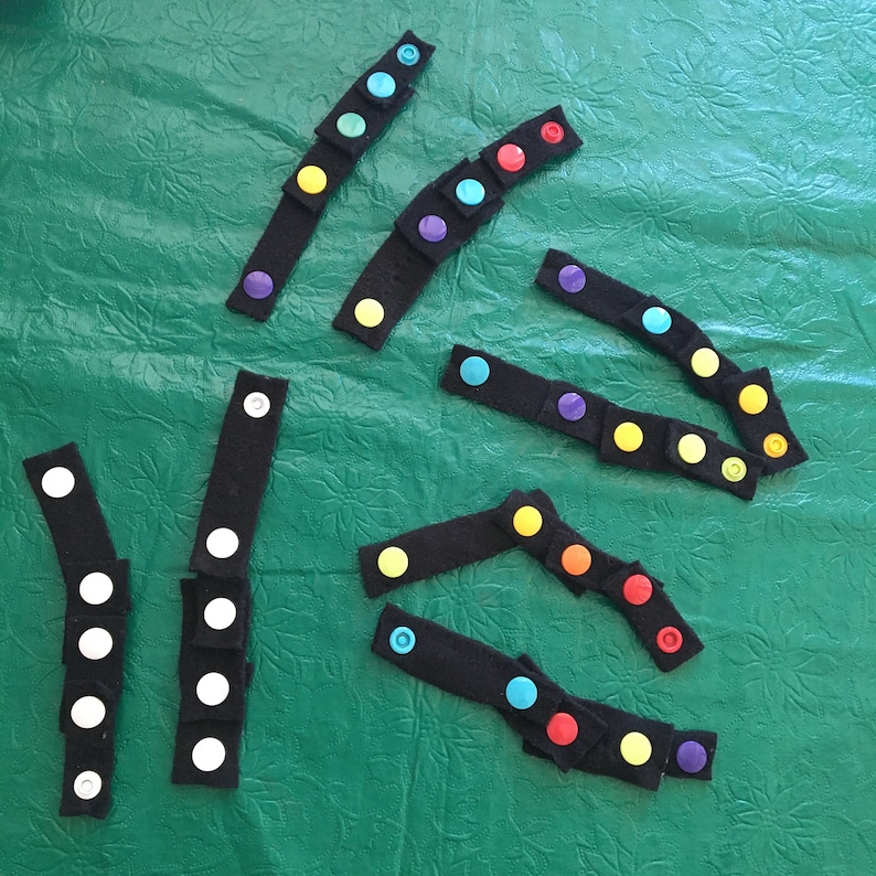 May include: Assortment of colorful felt strips with attached buttons. The strips are black with various colored buttons, including red, orange, yellow, green, blue, purple, and white.