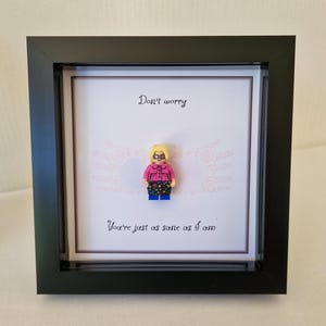 Może przedstawiać: Oprawiona grafika z figurką Lego w różowej koszuli i spodniach we wzory. Czarna ramka otacza białe tło z napisem "Don't worry, You're just as sane as I am."