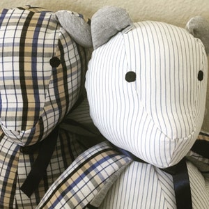 May include: Two plush teddy bears, one with a plaid pattern in shades of brown, beige, and blue, and the other with a white and blue striped pattern. Both bears have black button eyes and are tied with black ribbon.
