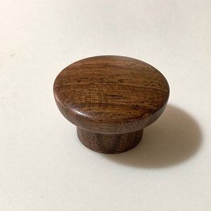 May include: A round wooden knob with a dark brown finish. The knob has a smooth, polished surface and a slightly raised edge.