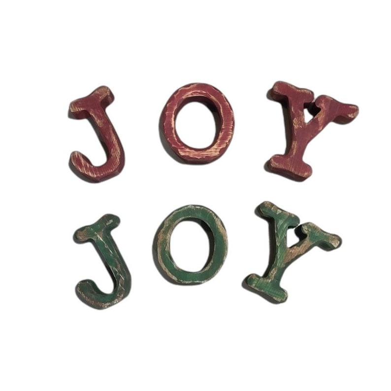 Puede incluir: Letras de madera que deletrean "JOY" en dos filas. La fila superior tiene una "J", "O" y "Y" rojas con detalles dorados. La fila inferior tiene una "J", "O" y "Y" verdes con detalles dorados. Las letras est&aacute;n ligeramente desgastadas.