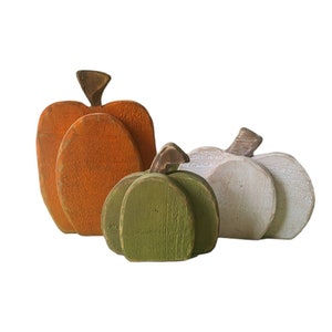 May include: Three wooden pumpkins in different sizes and colours. The largest pumpkin is orange, the middle pumpkin is green, and the smallest pumpkin is white.