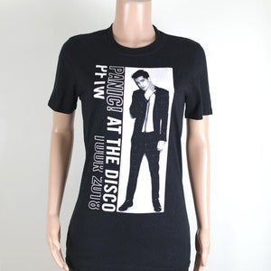 Könnte beinhalten: Schwarzes T-Shirt mit einem weißen Aufdruck eines Mannes im Anzug. Der Aufdruck lautet "Panic! At The Disco" und "P!ATW | U.U.U.K. 2018".