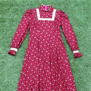 May include: A long-sleeved, red floral dress with a white lace trim around the neckline and cuffs. The dress has a high neck and a fitted bodice. The skirt is full and flowing.