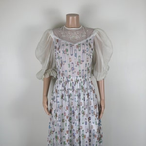 May include: A white dress with a geometric pattern of colorful sequins. The dress has a sheer overlay with a floral design and puff sleeves.