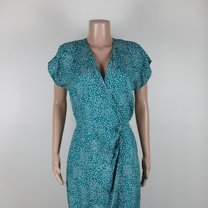 May include: A teal blue wrap dress with a white abstract print. The dress has a V-neckline and short sleeves.