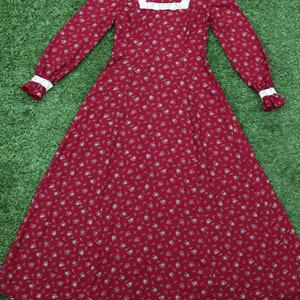 May include: A long-sleeved, red floral dress with a white lace collar and cuffs. The dress has a fitted bodice and a flowing skirt.