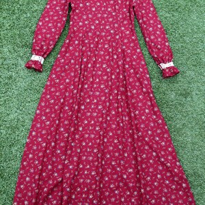 May include: A long-sleeved, red floral dress with a high neck and white lace trim on the cuffs. The dress has a full skirt and a small floral print.