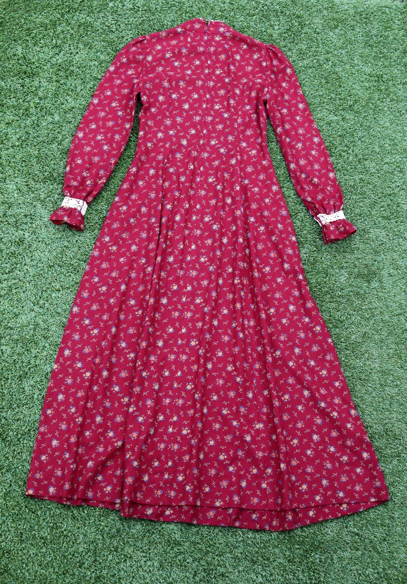 May include: A long-sleeved, red floral dress with a high neck and white lace trim on the cuffs. The dress has a full skirt and a small floral print.