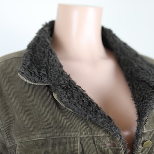 May include: A green corduroy jacket with a brown faux fur collar. The jacket has a button closure and two pockets.