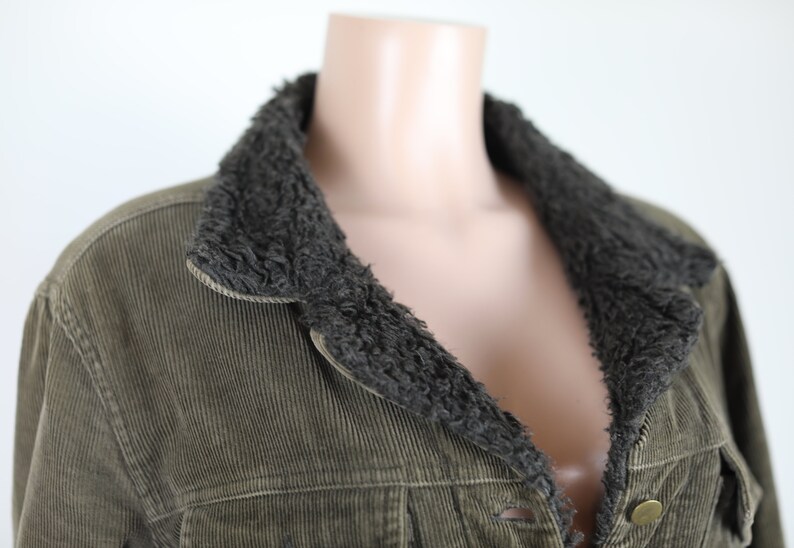 May include: A green corduroy jacket with a brown faux fur collar. The jacket has a button closure and two pockets.