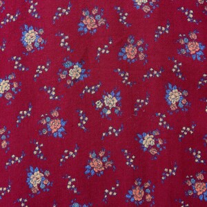 May include: Red fabric with a small floral pattern in shades of blue, pink, and white.