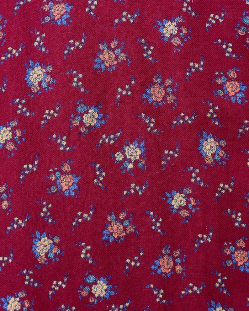May include: Red fabric with a small floral pattern in shades of blue, pink, and white.