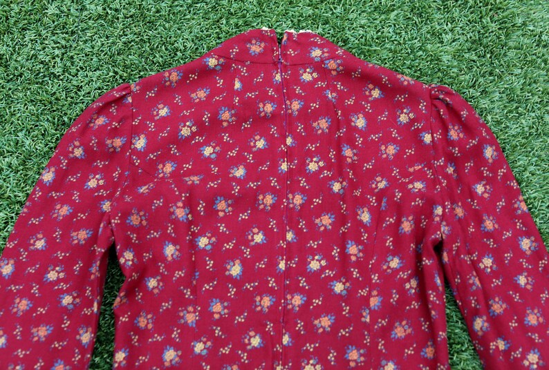May include: A red dress with a small floral print. The dress has a high neck and long sleeves.