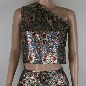 May include: A two-piece outfit with a gold, blue, and red paisley pattern. The top is a one-shoulder crop top and the bottom is a skirt.