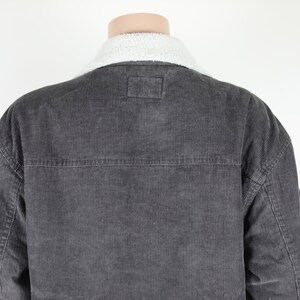 May include: A dark gray corduroy jacket with a white sherpa collar. The jacket has a button closure and two pockets on the front.