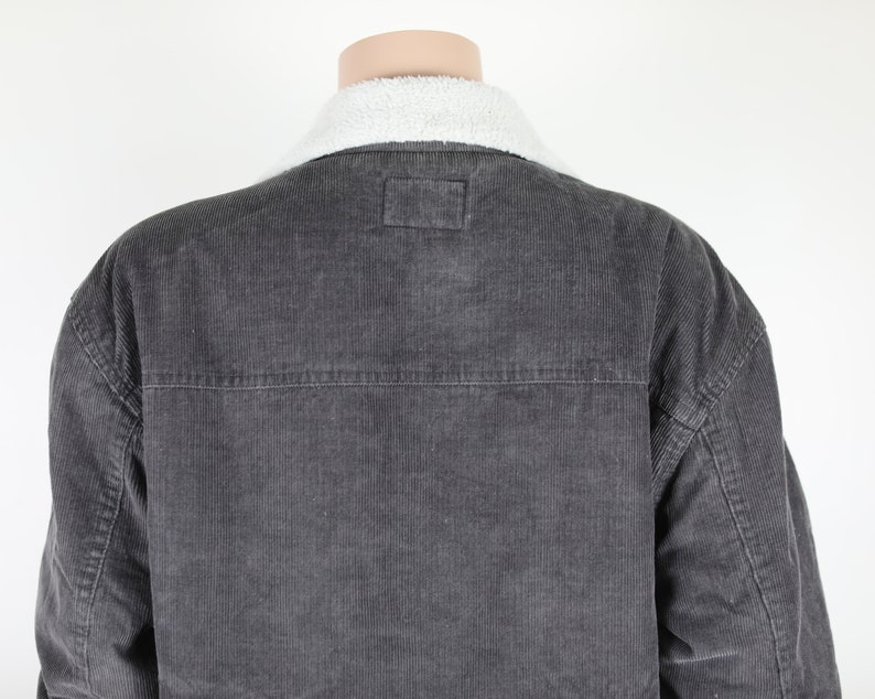 May include: A dark gray corduroy jacket with a white sherpa collar. The jacket has a button closure and two pockets on the front.