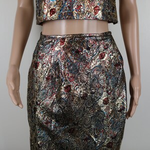 May include: A gold, red, and blue brocade crop top and skirt set. The fabric has a paisley-like pattern.