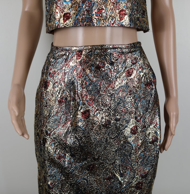 May include: A gold, red, and blue brocade crop top and skirt set. The fabric has a paisley-like pattern.