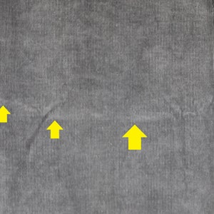 May include: Close-up of a gray corduroy fabric with three yellow arrows pointing upwards.