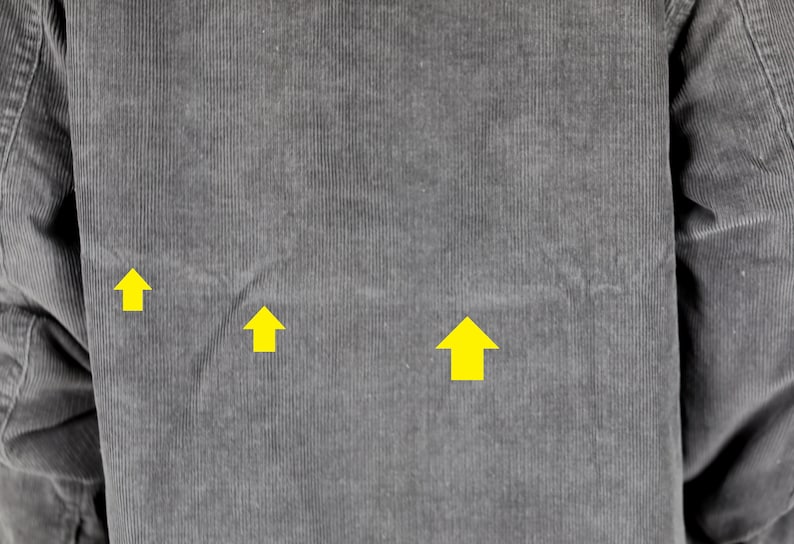 May include: Close-up of a gray corduroy fabric with three yellow arrows pointing upwards.