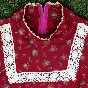 May include: Close-up of a red floral dress with white lace trim around the neckline. The dress has a pink zipper in the back.