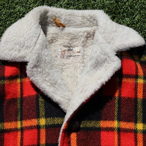 May include: Red, black and yellow plaid jacket with a white faux fur collar. The jacket has a button fastening and a label that reads "Sportswear".