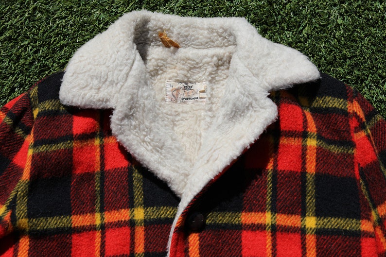 May include: Red, black and yellow plaid jacket with a white faux fur collar. The jacket has a button fastening and a label that reads "Sportswear".