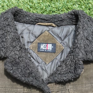 May include: A brown corduroy jacket with a black faux fur collar. The jacket has a diamond-shaped patch on the front that says "Miss Sixty" and "Made in China".