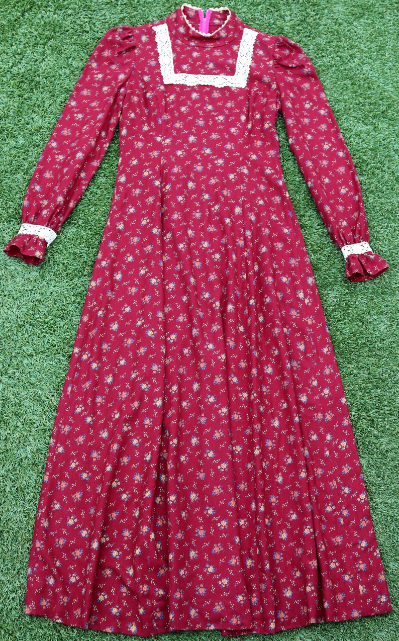 May include: A long-sleeved, red floral dress with a white lace collar and cuffs. The dress has a high neck and a fitted bodice. The skirt is full and flowing.