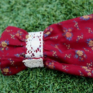 May include: Red fabric with a floral pattern and white lace trim. The fabric is gathered at the top and the lace trim is at the bottom.