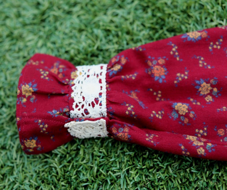 May include: Red fabric with a floral pattern and white lace trim. The fabric is gathered at the top and the lace trim is at the bottom.