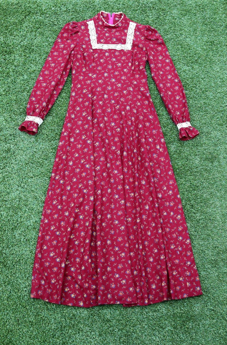May include: A long-sleeved, red floral dress with a white lace trim around the neckline and cuffs. The dress has a high neck and a fitted bodice. The skirt is full and flowing.