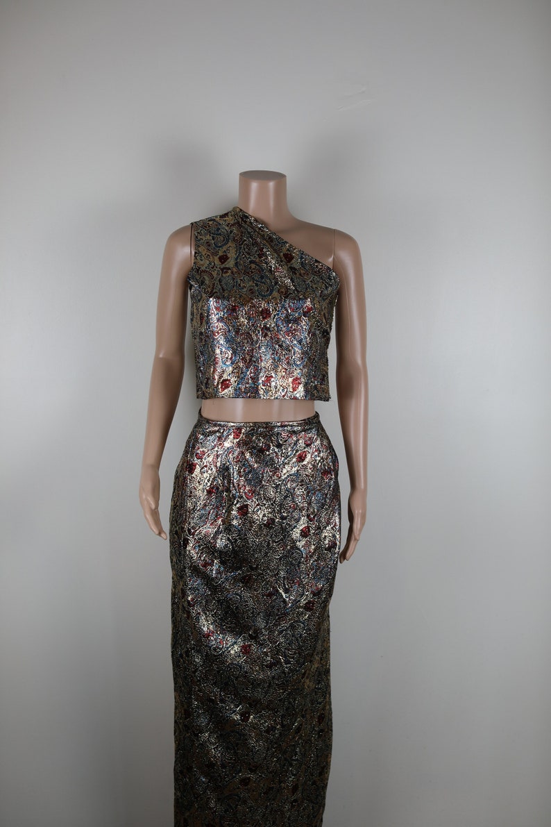 May include: A gold, red, and blue patterned two-piece outfit with a one-shoulder crop top and a long skirt.