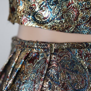 May include: A two-piece outfit with a gold, blue, and red paisley pattern. The top is a crop top and the skirt is a high-waisted skirt.