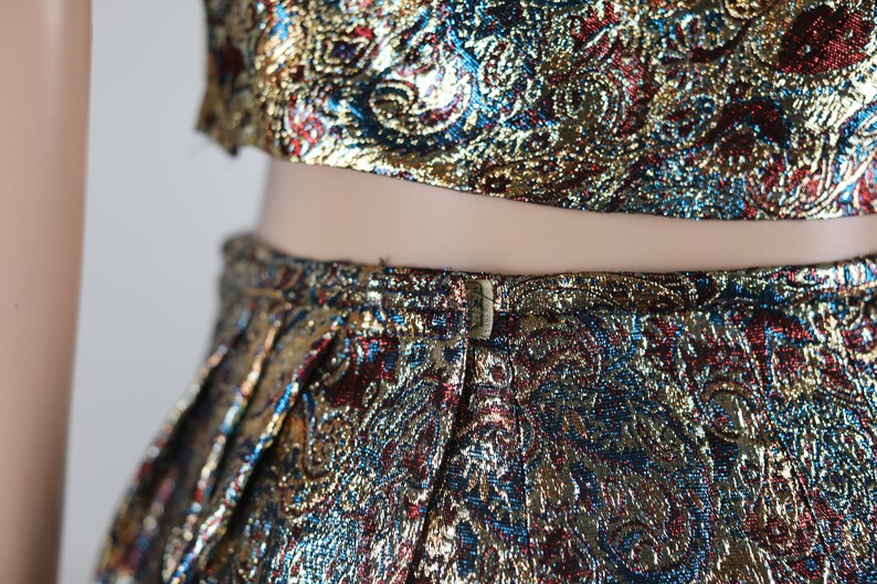 May include: A two-piece outfit with a gold, blue, and red paisley pattern. The top is a crop top and the skirt is a high-waisted skirt.