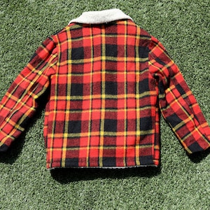 May include: A red, black and yellow plaid jacket with a white faux fur collar. The jacket is made of a soft, fuzzy material and has a button-up closure.