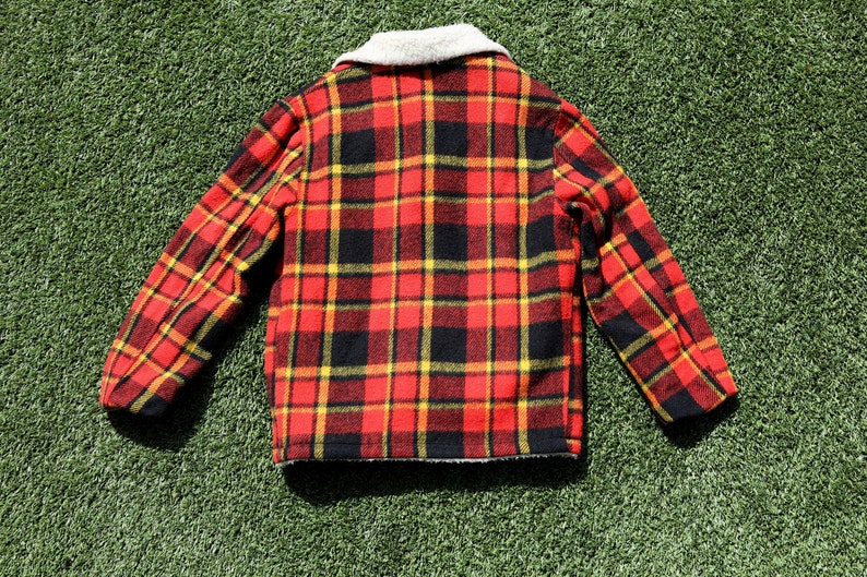 May include: A red, black and yellow plaid jacket with a white faux fur collar. The jacket is made of a soft, fuzzy material and has a button-up closure.