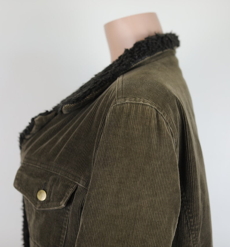 May include: A brown corduroy jacket with a black faux fur collar. The jacket has a button closure and a pocket on the left side.