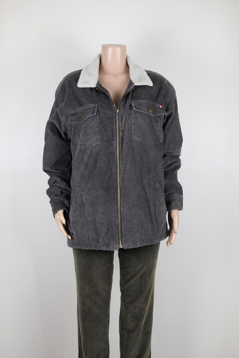 May include: A gray corduroy jacket with a white faux fur collar and a zipper closure. The jacket has two flap pockets on the chest and two pockets at the waist.