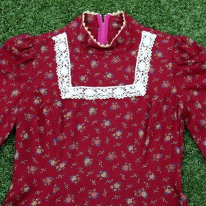 May include: A long-sleeved red dress with a white lace trim around the neckline. The dress has a small floral pattern.