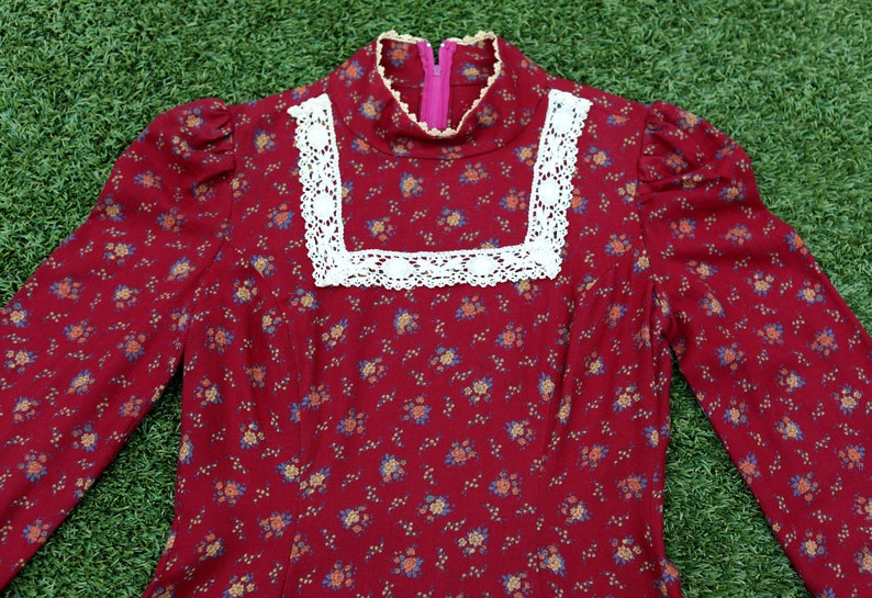 May include: A long-sleeved red dress with a white lace trim around the neckline. The dress has a small floral pattern.