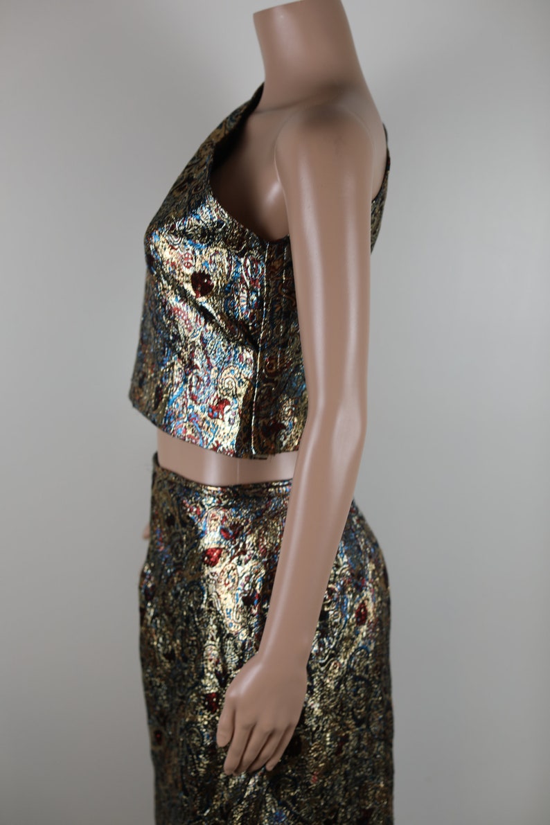 May include: A two-piece outfit with a gold, blue, and red patterned design. The top is a cropped, one-shoulder style. The skirt is a midi length.