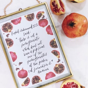 Peut inclure: Une impression encadrée en or avec un fond blanc et un texte de calligraphie noire. Le texte dit "Le Prophète Muhammad a dit : "Il n'y a pas de grenade qui n'ait pas un pépin provenant d'une des grenades du jardin (du Paradis) en elle." Abou Nou'aïth". L'impression est entourée d'illustrations à l'aquarelle de grenades.