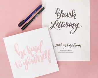 Puede incluir: Dos tarjetas blancas con letras negras de pincel. La tarjeta superior dice "Brush Lettering" de Darling Daydream, letras y diseño. La tarjeta inferior dice "Be Kind to Yourself" en letras rosas.