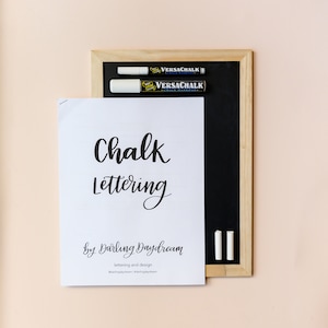 May include: A white sheet of paper with the text "Chalk Lettering by Darling Daydream lettering and design @darlingdaydream #darlingdaydream" on it. Two white chalk markers and a black chalkboard are on the right side of the paper.