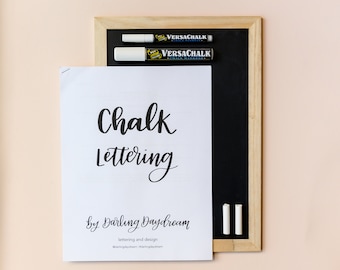 May include: A white sheet of paper with the text "Chalk Lettering by Darling Daydream lettering and design @darlingdaydream #darlingdaydream" on it. Two white chalk markers and a black chalkboard are on the right side of the paper.