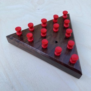 May include: A wooden triangular game board with 15 red pegs. The board is made of dark wood and has a hole in the center.