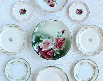 May include: A set of nine vintage floral plates in various sizes. The plates feature a white background with delicate floral designs in shades of pink, red, and green. The plates are perfect for adding a touch of vintage charm to any table setting.