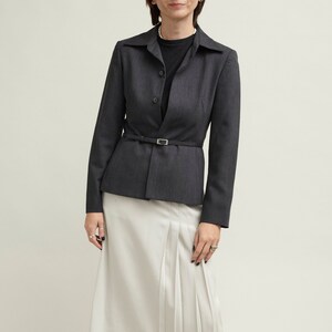 May include: A dark grey blazer with a black belt and a white pleated skirt. The blazer has a button-up front and long sleeves. The skirt is knee-length and has a slight A-line shape.